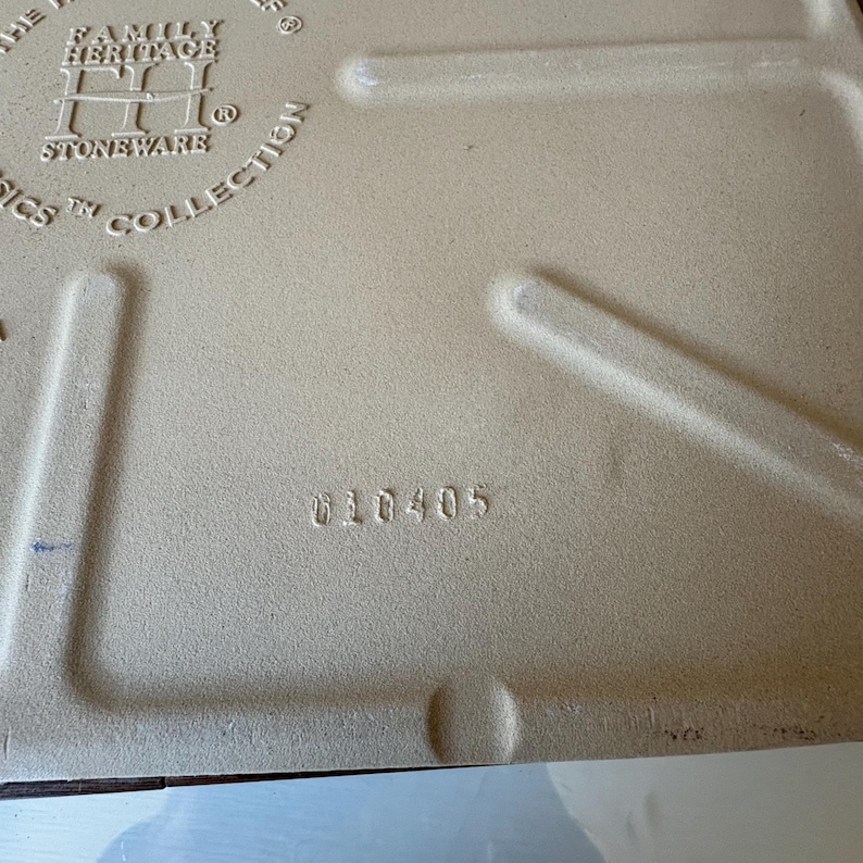 Puede incluir: Primer plano de la parte posterior de una pieza de gres. La superficie es de color beige claro con el texto "THE FAMILY HERITAGE STONEWARE CLASSICS COLLECTION" y el n&uacute;mero "010405" impresos.