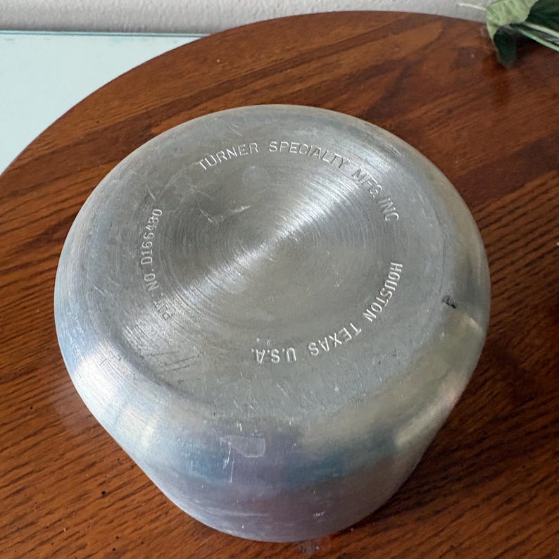 May include: A close-up of the bottom of a silver metal container. The text "TURNER SPECIALTY MFG INC HOUSTON TEXAS U.S.A." is visible. The patent number D166430 is also visible.