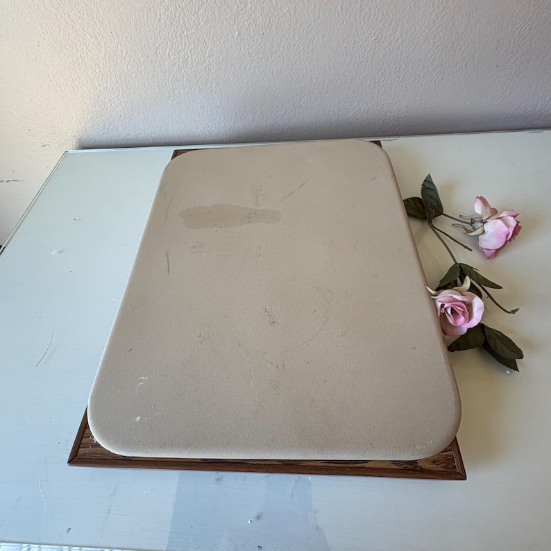 Puede incluir: Una bandeja rectangular, de color crema, con esquinas redondeadas, colocada sobre una base de madera oscura. La bandeja tiene una superficie ligeramente texturizada. Rosas rosas con hojas verdes se colocan en el lateral.