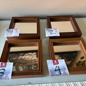 May include: Four small, square, wooden framed mirrors. Each mirror has a dark brown frame and a reflective surface. The mirrors are numbered 1 through 4 with small white tags. The mirrors are displayed on a light-colored surface.
