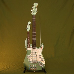 May include: A double-necked electric guitar with a green finish. The guitar has two necks, one with six strings and one with four strings. The guitar has a variety of knobs and switches on the body.