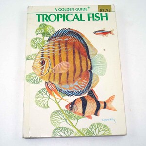 May include: A Golden Guide book titled "Tropical Fish" featuring colorful illustrations of various tropical fish species. The cover art includes a large orange and brown discus fish, a smaller fish with black stripes, and other aquatic plants.