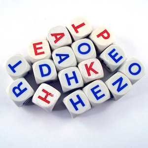 May include: A collection of white wooden dice with letters in red and blue. The dice are scattered, with some letters visible, spelling out words. The dice are on a white surface.