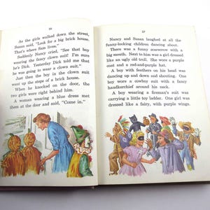 May include: A group of children dressed in Halloween costumes, including a clown, a scarecrow, a fairy, a cowboy, and a fireman. The children are dancing and laughing in front of a brick house.