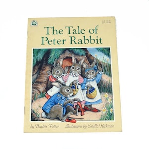 May include: A well-loved copy of "The Tale of Peter Rabbit" by Beatrix Potter. The cover shows an illustration of four rabbits, one in a blue jacket, and three in white aprons, carrying baskets of blueberries. The book has a cream-colored cover with the title in green.