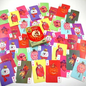 May include: A vintage "Crazy Faces" card game with numerous playing cards scattered around a red and green box. The cards feature colorful illustrations of whimsical characters, including clowns, pumpkins, and monkeys. The box reads "Bunny Rabbit Crazy Faces Card Game" and "29¢".