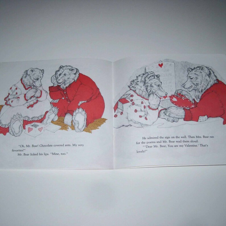 May include: An open book with illustrations of bears in a children's story. One bear is wearing a red outfit, and the other is wearing a white outfit with red accents. Text includes "Oh, Mr. Bear! Chocolate covered ants. My very favorites!" and "Dear Mr. Bear, You are my Valentine."
