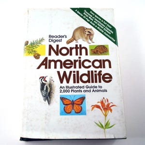 May include: A Reader's Digest North American Wildlife hardcover book featuring illustrations of a raccoon, turtle, woodpecker, monarch butterfly, and orange lily. The cover text reads: An Illustrated Guide to 2,000 Plants and Animals.