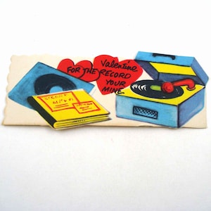 May include: A vintage Valentine's Day card featuring a blue and yellow record player with a red tone arm. The card also includes a record album, a record in a blue sleeve, and two red heart shapes with the text "For the record your mine."
