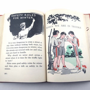 May include: An open book with illustrations and text. One page shows a person writing "SAFETY RULES FOR WINTER" on a chalkboard. The other page shows three boys. Text discusses winter safety.