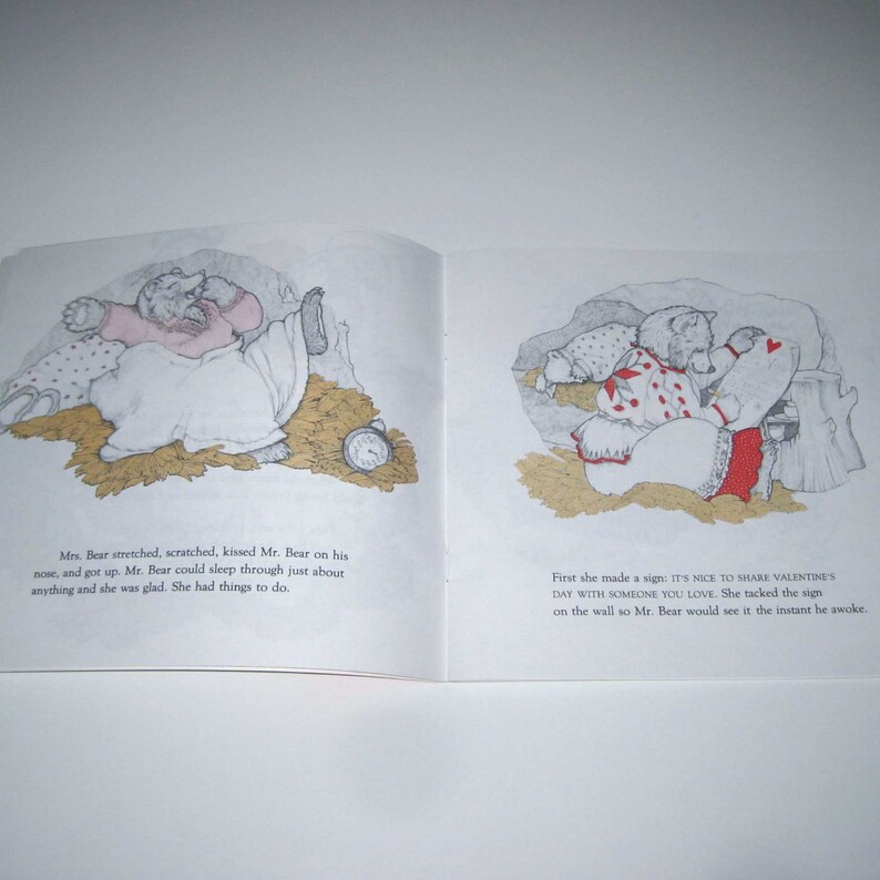 May include: An open book with illustrations of bears in a cozy setting. One image shows a bear in bed with an alarm clock. The other shows a bear with a sign that reads, "IT'S NICE TO SHARE VALENTINE'S DAY WITH SOMEONE YOU LOVE."