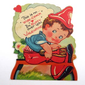 May include: A vintage Valentine's Day card featuring a cartoon boy in a red hat and overalls riding a red toy fire truck. The card has the text "This is no... WISE-CRACK I'm NUTTY over you VALENTINE" on it.