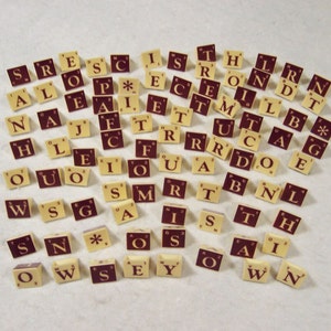 May include: A collection of letter tiles in a cream color with brown lettering. The tiles are arranged in a random pattern and include letters of the alphabet, numbers, and a blank tile with an asterisk.