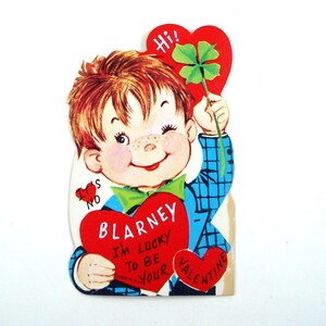 May include: Vintage Valentine's Day card featuring a cartoon boy winking and holding a four-leaf clover and a red heart. The heart reads "Blarney I'm Lucky to Be Your Valentine". The boy wears a blue plaid jacket and a green bow tie.