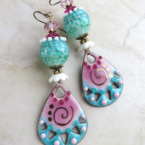 Può includere: Orecchini pendenti artistici con una combinazione di colori turchese e rosa. Gli orecchini presentano una forma a goccia con un design a spirale e una parte superiore con perline. Realizzati con metallo e perline di vetro.