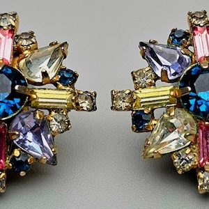 Puede incluir: Un par de pendientes de tono dorado con un diseño de estrella. Los pendientes están adornados con diamantes de imitación transparentes, rosas, azules y morados.
