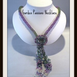 May include: A beaded necklace on a white bust form. The necklace is primarily purple and green, with a central oval pendant and a beaded tassel. The text "Garden Passions Necklace" is above the necklace. The text "A Pattern For Personal Use" and "By Hannah Rosner" are below.