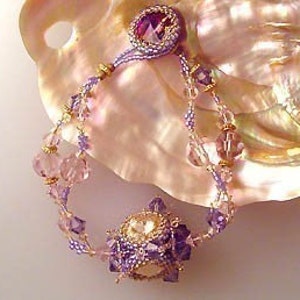 K&ouml;nnte beinhalten: Ein Armband mit Perlen und einem violetten und wei&szlig;en Kristall als Mittelpunkt. Das Armband ist aus klaren und rosafarbenen Perlen gefertigt und hat einen goldenen Akzent.