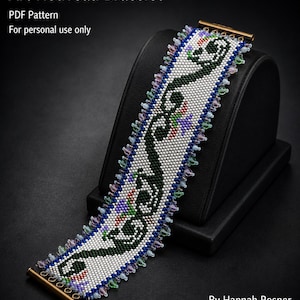 Op de afbeelding: Een brede kralenarmband met een witte achtergrond en een donkergroen vloeiend patroon, geaccentueerd door kleine rode en paarse details. De randen zijn afgewerkt met kleine lichtblauwe, roze en groene kralen. Tekst: Art Nouveau Bracelet PDF Pattern.