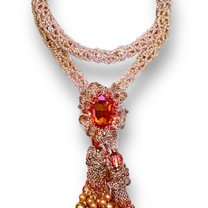 May include: A handcrafted necklace featuring a beaded design in shades of gold, peach, and orange. The necklace has a large, oval-shaped orange gemstone pendant with a beaded tassel. The necklace is approximately 18 inches long.