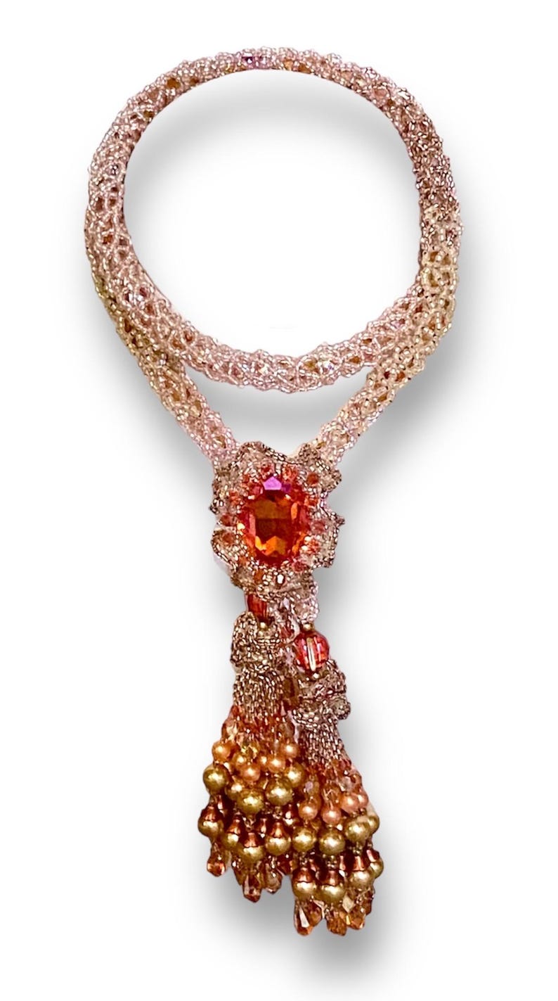 May include: A handcrafted necklace featuring a beaded design in shades of gold, peach, and orange. The necklace has a large, oval-shaped orange gemstone pendant with a beaded tassel. The necklace is approximately 18 inches long.