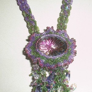 May include: A handmade beaded necklace featuring a large, oval-shaped pendant with a central iridescent stone. The necklace incorporates shades of purple, green, and clear beads, creating a detailed and ornate design. The necklace is a unique piece of jewelry.