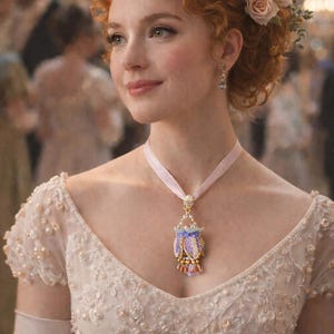May include: A woman in an elegant white gown, adorned with pearls and a decorative necklace. She wears a tiara and flowers in her hair. The background is blurred, suggesting a formal event or ball.