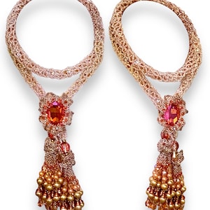 May include: Two beaded necklaces with a circular design. Each necklace features a large, oval-shaped orange gemstone pendant, intricate beadwork, and a tassel of golden beads. The necklaces are displayed against a white background.