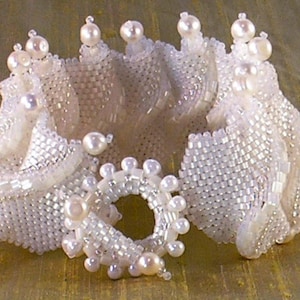 Puede incluir: Un brazalete de cuentas blancas con un dise&ntilde;o delicado e intrincado. El brazalete est&aacute; hecho de peque&ntilde;as cuentas blancas que se tejen juntas para crear una forma fluida y org&aacute;nica. El brazalete est&aacute; acentuado con cuentas blancas m&aacute;s grandes que a&ntilde;aden un toque de brillo.
