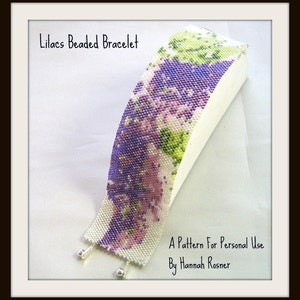 Op de afbeelding: Lila Perlen Armband, een kralenarmband met een paars, groen en wit bloemenpatroon. De armband ligt op een wit oppervlak. Een patroon voor persoonlijk gebruik door Hannah Rosner.