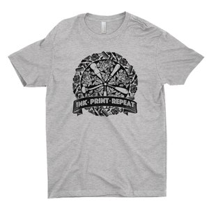 May include: A gray t-shirt with a black and white graphic design of printing tools and flowers. The graphic includes the text "INK PRINT REPEAT".