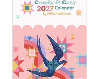 May include: A wall calendar titled Comfy & Cozy 2027 Calendar by Mirka Hokkanen. The cover features a dark blue bird in flight against a light pink background, decorated with colourful geometric star patterns and a rainbow arch graphic.