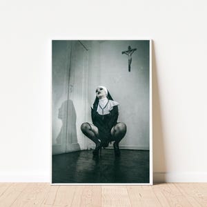 Può includere: Stampa incorniciata in bianco e nero raffigurante una persona in abito da suora, inginocchiata. Un crocifisso è appeso al muro. L'immagine ha un'estetica drammatica e ad alto contrasto.