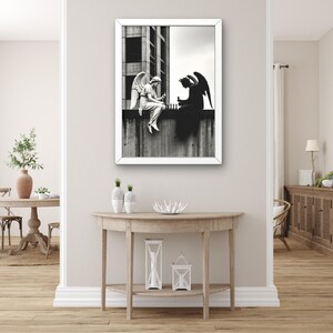 Puede incluir: Impresión en blanco y negro enmarcada que representa a un ángel y un diablo jugando al ajedrez en una repisa de hormigón. El ángel está sentado, el diablo está silueteado. La obra de arte se exhibe sobre una consola de madera con jarrones y linternas decorativas.