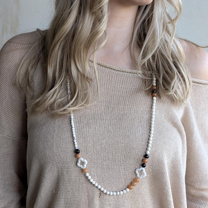 May include: A long white beaded necklace with brown and black beads and white flower-shaped charms.