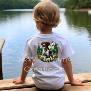 May include: A white t-shirt with a brown and white German Shorthaired Pointer dog illustration on the back. The dog is standing in a forest setting with ducks flying overhead. The text "J&W Custom Creations" is visible on the bottom of the shirt.