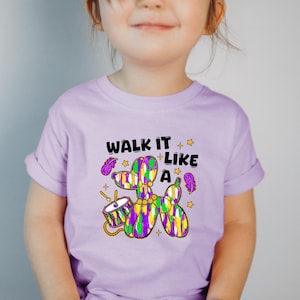 May include: A light purple t-shirt with a cartoon illustration of a purple, green, and gold balloon animal dog. The text "Walk it like a" is printed above the dog.