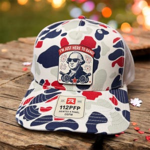 May include: A camouflage-patterned baseball cap with a white mesh back. The front features a patch with an image of George Washington wearing sunglasses and the text "I'M JUST HERE TO BANG!". The hat also has a label that reads "112PFP PRINTED 5 PANEL OSFM".