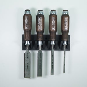 May include: Five wood chisels with wooden handles are mounted on a black wall rack. The chisels are labelled with the brand name "narex" and the size in millimetres. The chisels are made in the Czech Republic.