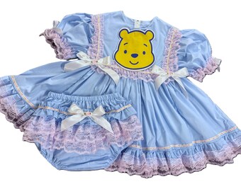 Può includere: Un set di vestito e mutandine per neonati azzurro chiaro. L'abito presenta una grafica di Winnie the Pooh, fiocchi bianchi e finiture in pizzo rosa. Il set è realizzato in tessuto morbido.