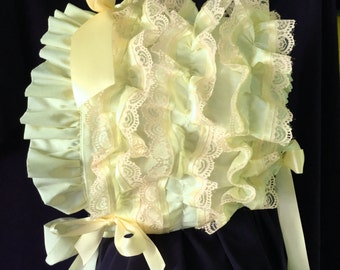 May include: A yellow baby bonnet with lace trim and satin ribbon ties. The bonnet is made of soft fabric and has a ruffled edge.