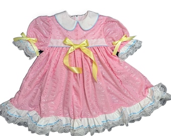 May include: A pink and white dress with yellow ribbon accents and lace trim. The dress has a peter pan collar and short sleeves.