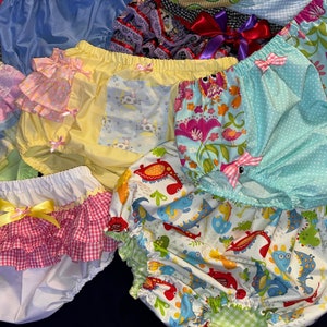 May include: A collection of colorful, patterned baby bloomers with ruffles. The bloomers are made of various fabrics and feature different designs, including floral, animal, and geometric patterns.