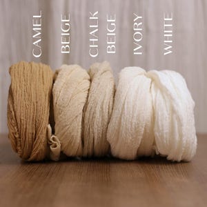 K&ouml;nnte beinhalten: F&uuml;nf Rollen aus strukturiertem Stoff, die in einer Reihe angeordnet und mit den Farben Camel, Beige, Chalk Beige, Ivory und White beschriftet sind. Jede Rolle weist eine knittrige, gazeartige Optik mit einer einheitlichen Webstruktur auf.