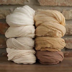 May include: A stack of four white, beige, and brown fabric wraps. The fabric is soft and textured, and the wraps are arranged in a neat pile.