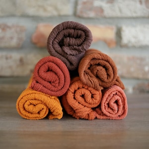 Peut inclure: Une pile de serviettes roulées de couleurs orange, rouille et marron. Les serviettes sont disposées en forme de pyramide, mettant en valeur leurs surfaces texturées. L'arrière-plan présente un mur de briques et une surface en bois.