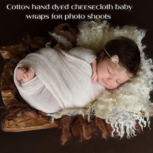 Può includere: Un neonato avvolto in un pannolino di mussola bianca, dorme su un tappeto soffice marrone e bianco. Il bambino indossa una fascia beige con un fiocco.