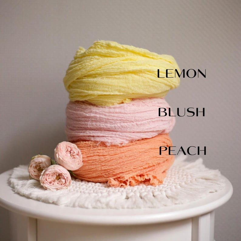 K&ouml;nnte beinhalten: Drei gestapelte Rollen aus strukturiertem Stoff in Zitronengelb, zartem Rosa und Pfirsichorange. Der Text LEMON, BLUSH und PEACH ist neben der jeweiligen Farbe aufgedruckt. Zwei kleine, hellrosa Rosenbl&uuml;ten liegen an der Basis des Stapels.