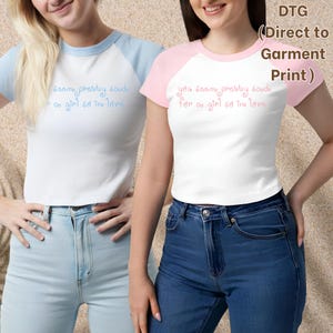 May include: Two raglan t-shirts with white bodies and colored sleeves. The left shirt has light blue sleeves and blue text, while the right shirt has pink sleeves and pink text. Both shirts feature the phrase you seem pretty sad for a girl so in love.