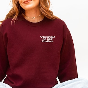 Könnte beinhalten: Ein weinrotes Sweatshirt mit dem Text "*kann spuren von Wein enthalten." in weißer Schrift. Das Rundhals-Sweatshirt ist einfarbig und hat lange Ärmel. Der Text befindet sich oben links auf der Brust.